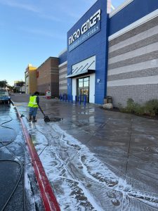 Commercial pressure washing in action at a Phoenix shopping center. A technician is using a hot-water surface cleaner to deep clean the concrete sidewalks, removing gum and heavy foot traffic stains.