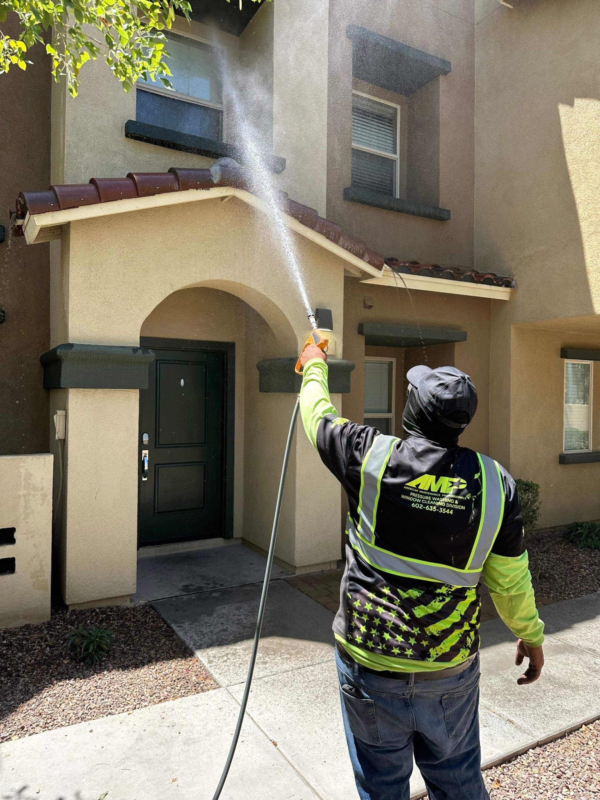 A residential house in Phoenix undergoing a professional house washing service. A technician is safely cleaning the stucco exterior, demonstrating a key topic from our homeowner's guide.